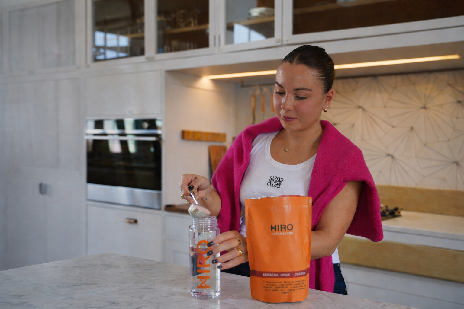 Woman mixing HIRO essential health supplement powder into a water bottle in a modern kitchen